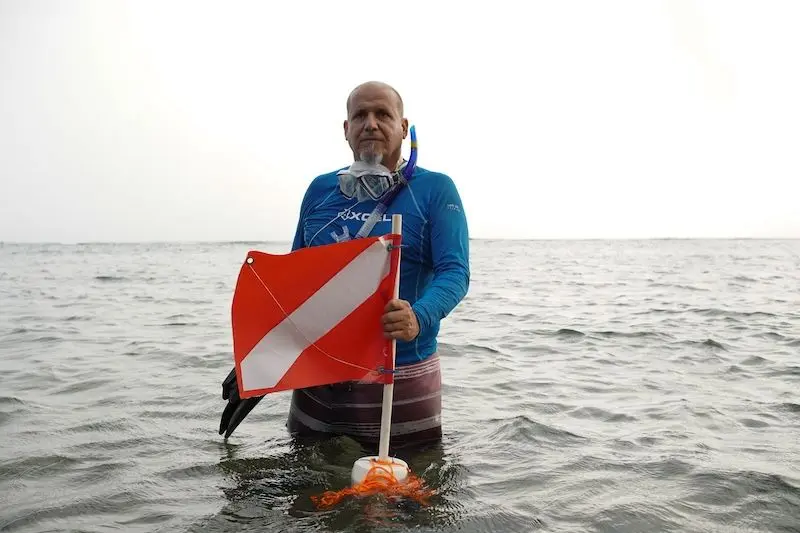 Ricardo Laureano sostiene una bandera de precaución con la que los buzos alertan a los barcos para guardar su distancia en las zonas donde hacen inmersiones. Foto: Gabriela Meléndez Rivera, Global Press Puerto Rico.